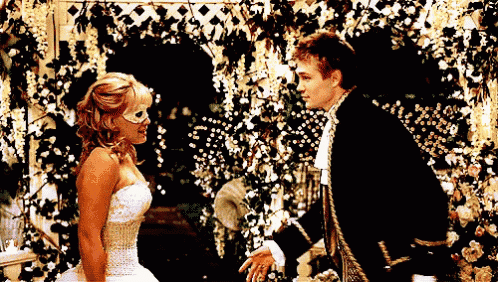 a man in a black suit and a woman in a white dress are looking at each other