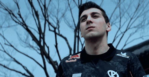 a man wearing a red bull shirt stands in front of trees