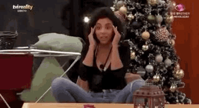 a woman is sitting on the floor in front of a christmas tree .