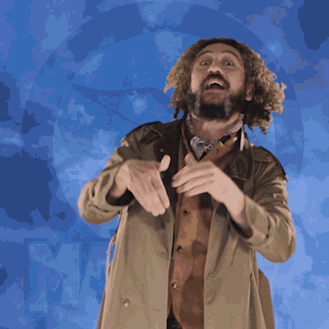 a man with a beard wearing a trench coat stands in front of a blue sky