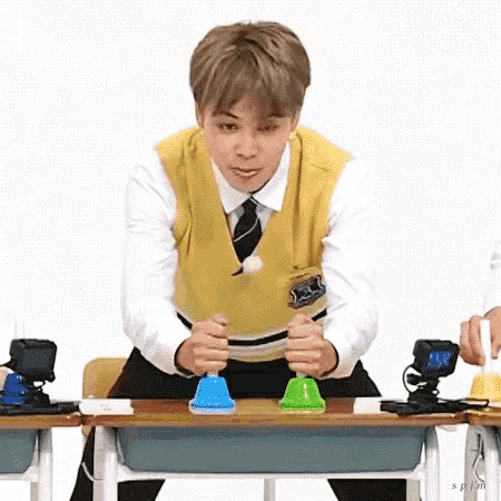 a young man in a yellow vest and tie is sitting at a desk playing with bells .