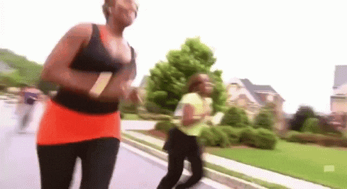 two women are jogging on a sidewalk in a neighborhood .