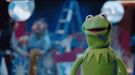 kermit the frog from the muppet show is standing in front of a ladder and looking at the camera .