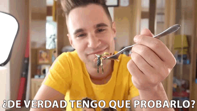 a man in a yellow shirt is holding a spoon in his mouth with the words de verdad tengo que probarlo below him