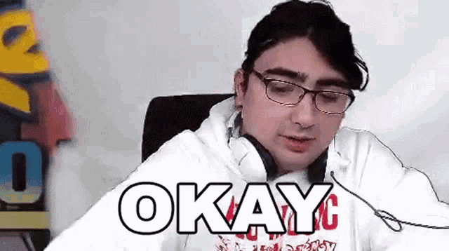 a man wearing glasses and headphones is sitting in a chair with the word okay written on his shirt .