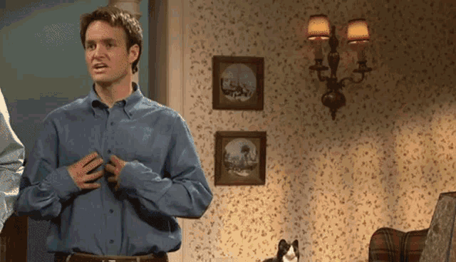 a man in a blue shirt is standing in a living room with pictures on the wall