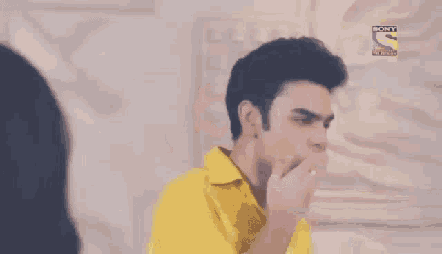 a man in a yellow shirt is standing in front of a wall with a sony logo on it