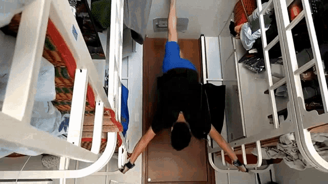 a man in a blue shirt is doing a handstand in a room with bunk beds