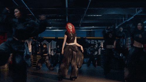 a woman with red hair is dancing in a dark room with a sign that says ' n ' on it