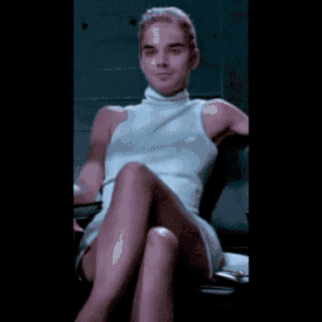 a man in a white tank top is sitting in a chair with his legs crossed