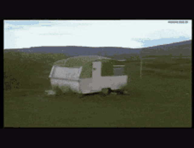 a white trailer with a green roof is parked in a field