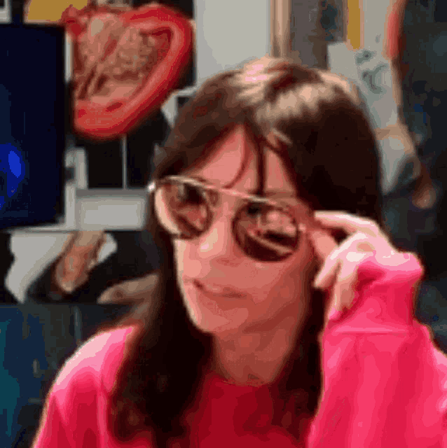 a woman wearing sunglasses and a pink sweater looks at the camera