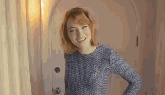 a woman in a blue dress is standing in front of a white door and smiling .
