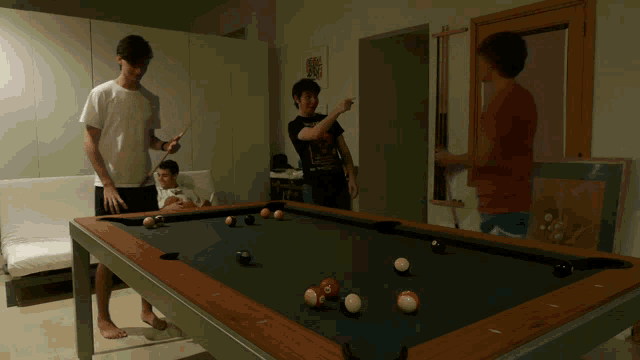 a man wearing a t-shirt with a skull on it is playing pool with two other men