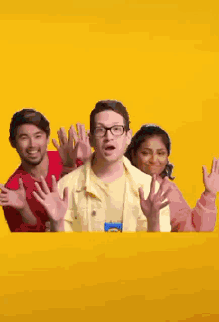 a group of people are standing next to each other and waving their hands in front of a yellow background .
