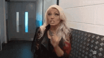 a woman is standing in a hallway with her hands folded and making a funny face .