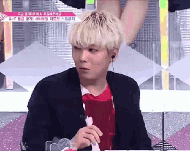 a man with blonde hair is sitting at a table with a microphone