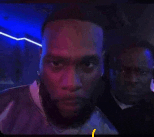 a man with a beard is standing next to another man in a dark room with blue lights .