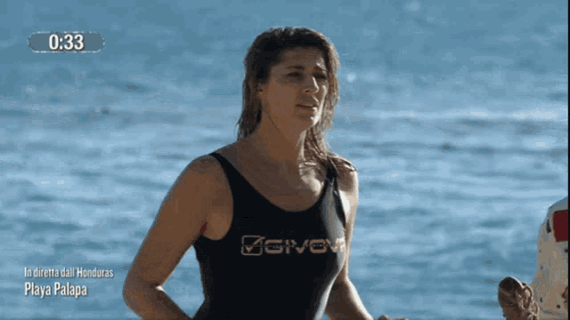 a woman in a givova swimsuit stands in front of a body of water
