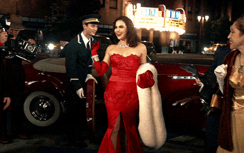 a woman in a red dress and fur coat stands in front of a theatre
