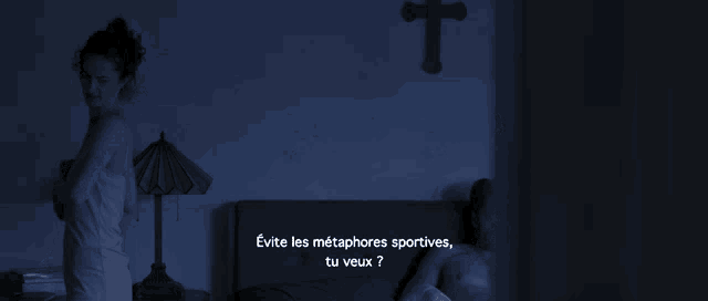 a dark room with a cross on the wall and a woman standing next to a man in bed