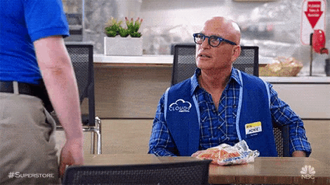 a man in a blue vest is sitting at a table with a bag of chips on it .