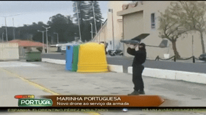 a man is holding a small drone in front of a sign that says portugal