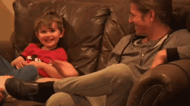 a man and a child are sitting on a couch playing with each other .