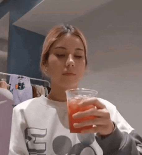 a woman in a mickey mouse sweatshirt is holding a cup of juice