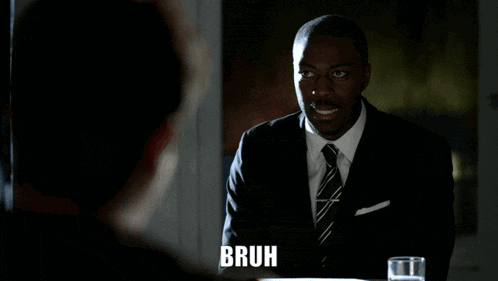 a man in a suit and tie is sitting at a table with the word bruh above him