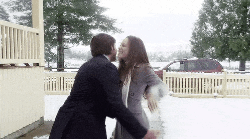 a man and a woman are hugging in the snow in front of a fence .