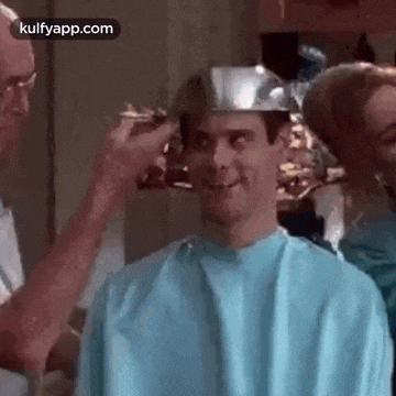 a man is getting his hair cut in a barber shop while wearing a metal hat .