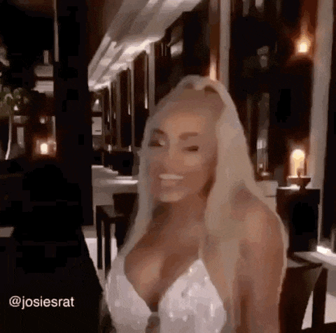 a blonde woman in a white dress is smiling in a room .