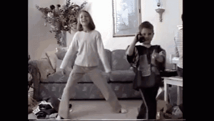 a boy and a girl are dancing in a living room while a boy takes a picture of them .