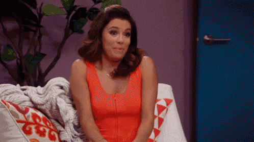 a woman in a red dress is sitting on a couch making a funny face .