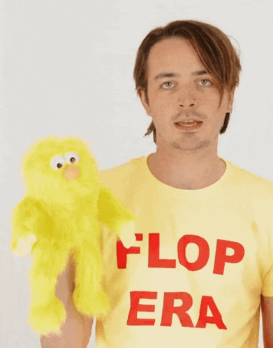 a man wearing a yellow flop era shirt holds a yellow stuffed animal