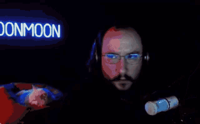 a man wearing glasses and headphones stands in front of a neon sign that says donmoon