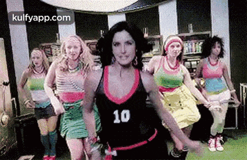a group of women are dancing together in a room . one of the women is wearing a number 10 tank top .