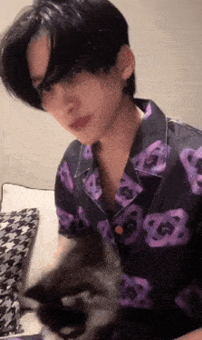 a young man in a purple shirt is petting a cat .