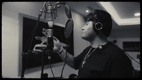 a man wearing headphones is singing into a microphone with a key necklace around his neck