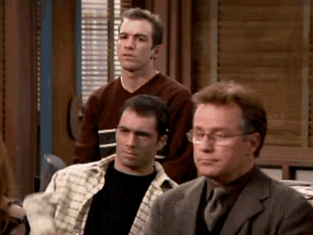 a group of men are sitting in a room and one of them has glasses on