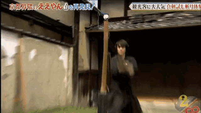 a man is holding a sword in front of a building with the number 2 on the bottom right corner