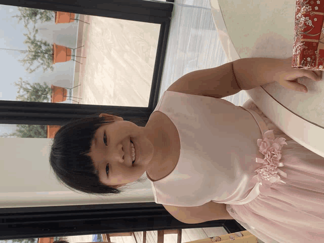a little girl in a pink dress sits at a table smiling