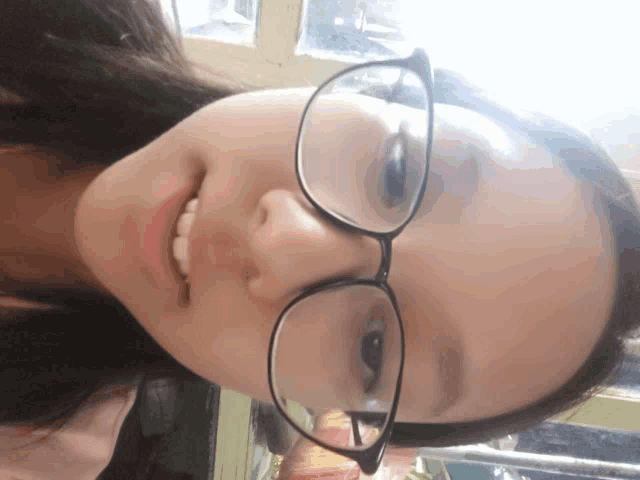 a girl wearing glasses looks down at the camera