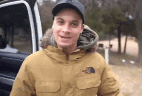 a man wearing a north face jacket is standing next to a car