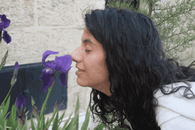 a woman smelling a purple flower with a brick wall in the background