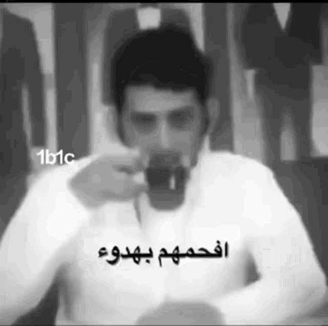 a black and white photo of a man drinking from a cup with arabic writing on it .