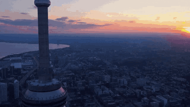 an aerial view of a city at sunset with a very tall tower in the foreground