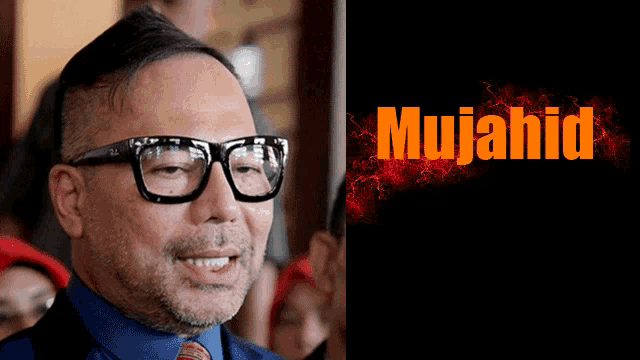 a man wearing glasses and a blue shirt next to a poster that says mujahid