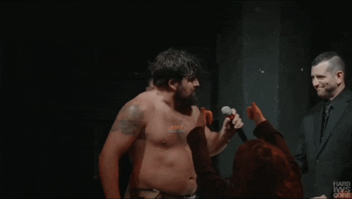 a man without a shirt is standing in a dark room with a hard iws core logo on the bottom